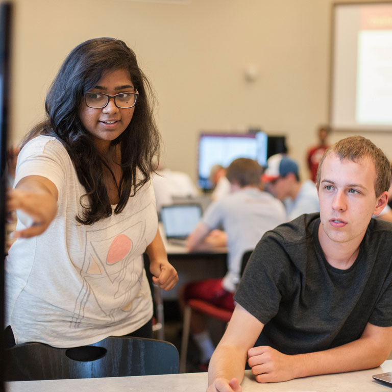 A student points to an explanation on a screen to help a fellow student.