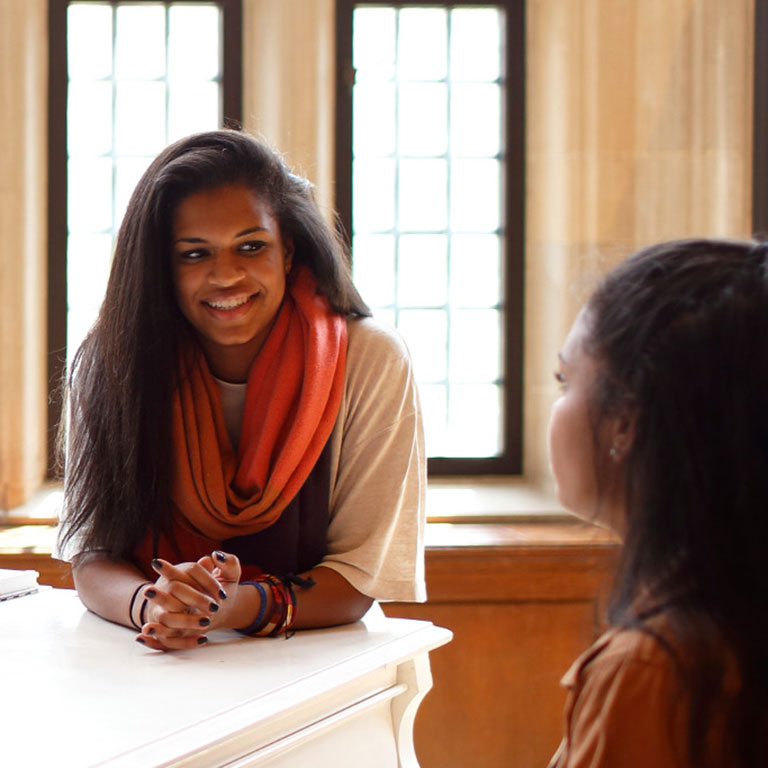 Two students talk while one student plays the piano.
